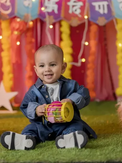 A happy baby boy celebrating Diwali in the studio. He is sitting on the floor playing with a traditional lantern amidst a colorful and brightly lit backdrop.