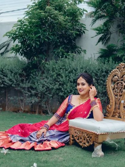 A full-length portrait of the bride relaxing on an ornate chair in a garden. Her vibrant half saree spreads out beautifully on the grass.