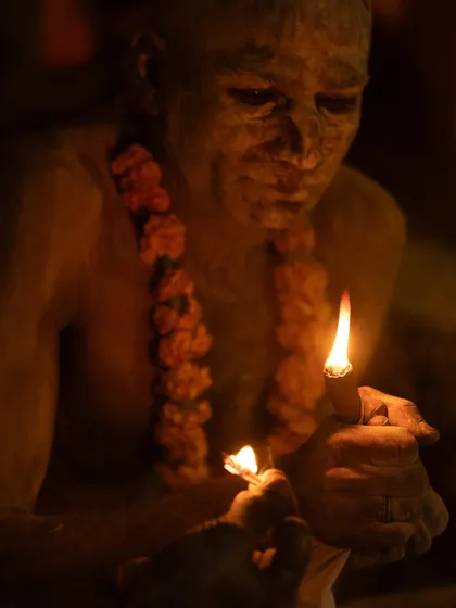A Naga sadhu lights his chillum in the dark, the two small flames creating an intimate and powerful source of light.