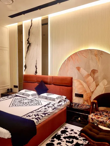 This angle shows the complete look of the master bedroom, with its bold rust-colored bed, custom headboard design, and a cozy corner chair for reading.