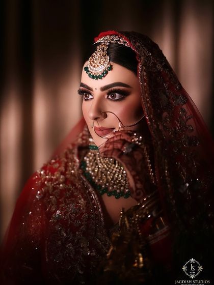 A close-up of this traditional bridal makeup, focusing on the rich color palette. The deep red lehenga is balanced with emerald jewelry and a makeup look that features a defined eye and flawless base.