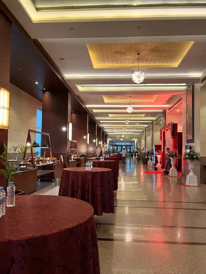 A long corridor in a luxury hotel, set up with cocktail tables for a pre-function gathering, leading to the main event entrance.