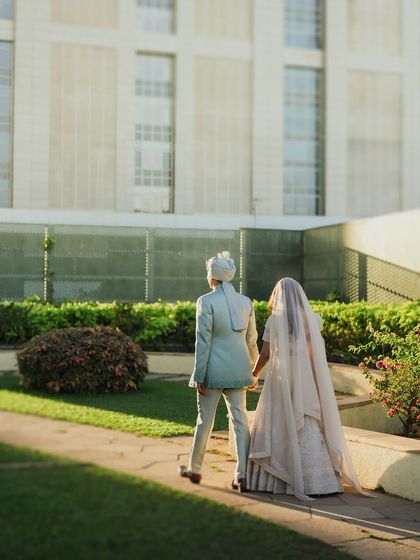 The couple walks away hand-in-hand, a classic "just married" moment captured in a modern urban setting. The clean architecture provides a beautiful contrast to their traditional attire.