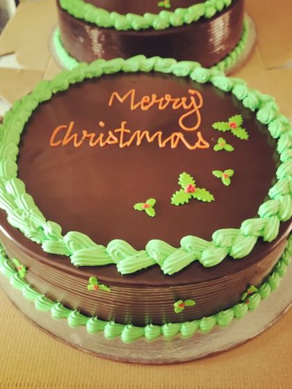 A classic chocolate truffle cake decorated for Christmas. The simple yet festive design with green frosting and holly leaves makes it a perfect addition to any holiday celebration.