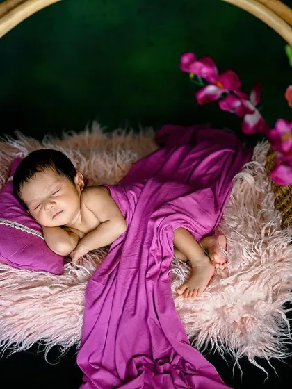 A smiling newborn in a hanging basket. The rich purple wrap and soft pink fur create a beautiful color combination.