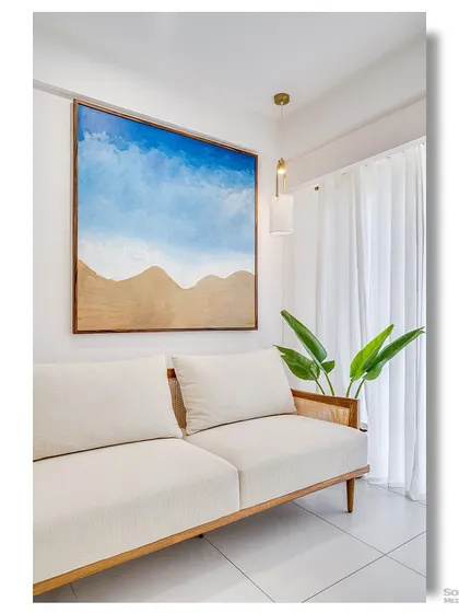 A simple and sophisticated seating area, where a minimalist white sofa is paired with a large abstract beach painting. The natural light and indoor plant enhance the room's fresh and calming ambiance.
