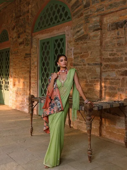 A full-length shot that captures the complete look. The floral print cape adds a contemporary layer to the traditional saree, showing a unique way to style ethnic wear.
