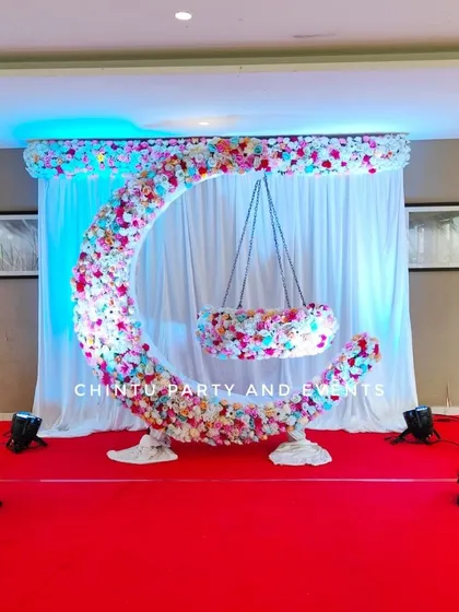 A stunning naming ceremony cradle decoration. The cradle is suspended within a large, moon-shaped structure completely covered in fresh flowers.