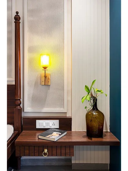 A close-up on the custom bedside table, showcasing the simple, clean design and the warm glow of the vintage-style wall lamp.