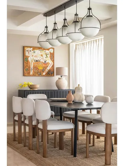 The dining room in Apartment 1600 captures a sense of tropical luxury. A dark wood table is paired with unique, block-legged chairs and a statement pendant light, with vibrant artwork adding a splash of color to the serene space.