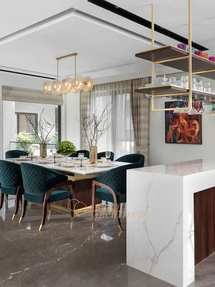 This combined dining and bar area is perfect for entertaining. The design features a marble-topped bar with an overhead rack for glasses and a dining table with plush green velvet chairs.
