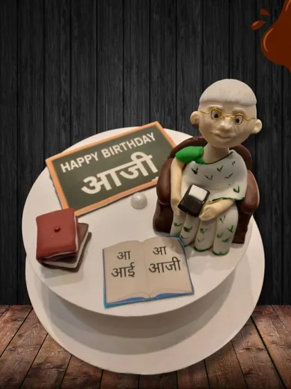 I made this special cake to celebrate an "Aaji" (grandmother). It features a sweet fondant figure of a grandmother teaching, complete with a book and a small blackboard, honoring her wisdom and love.
