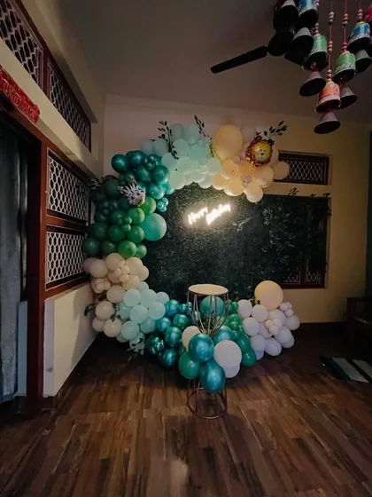 An elegant birthday setup with a half-arch of green, white, and cream balloons against a dark backdrop, complete with a 'Happy Birthday' neon sign.