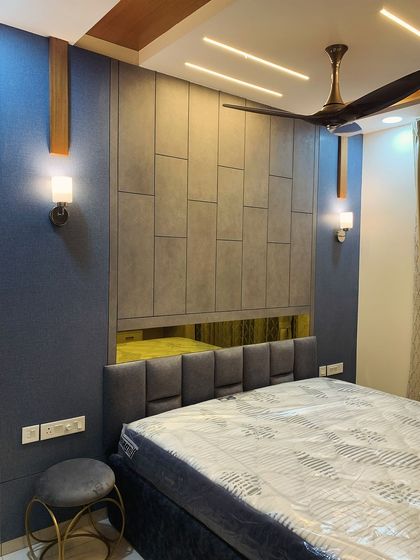 This elegant bedroom features a cot with a cushioned headboard set against a wall with textured panels. The tinted mirror and warm wall sconces add to the room's sophisticated ambiance.