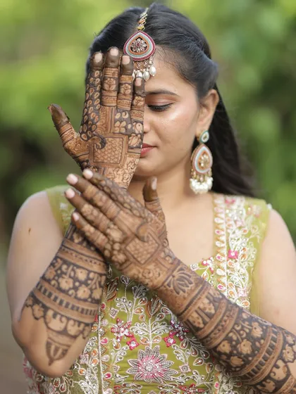 A classic and elegant pose, with the bride's mehendi-adorned hands partially covering her face. The detail in the henna is exquisite.