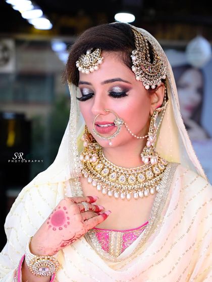 A classic bridal portrait showing the bride's elegant pose and the detailed craftsmanship of her white and pink lehenga.