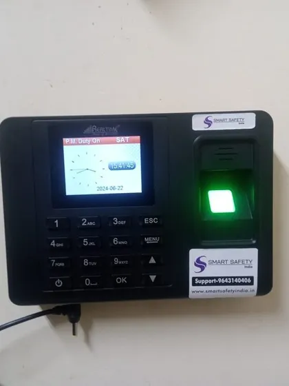 A newly installed Realtime biometric attendance system, ready for use. The clear screen displays the time and date, and the green light on the scanner indicates it's active.