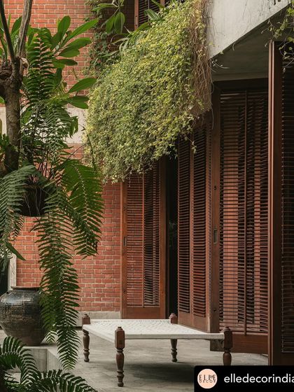 A simple woven charpoy sits in a covered verandah, surrounded by ferns and cascading creepers. This space was designed as a quiet outdoor lounge, perfect for enjoying the garden while being sheltered from the elements.