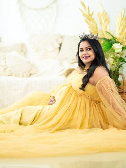 A beautiful portrait of a mom-to-be relaxing in a yellow gown on the floor of our studio. The wide shot captures the flowing fabric and the serene setting.