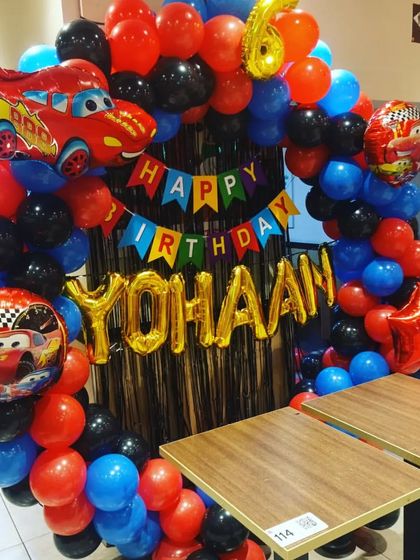 A high-energy Racing Cars theme perfect for any little speedster. This setup features a balloon ring in red, blue, and black, with Lightning McQueen foil balloons and a "Happy Birthday" banner.