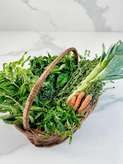 The heart of our kitchen is our farm. This basket, brimming with chemical-free leeks, baby carrots, kale, and fragrant herbs like sage and thyme, represents our commitment to fresh, high-quality produce, picked and delivered on the same day.