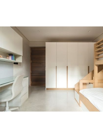 The kids' room is designed with plenty of storage, including a full-wall wardrobe and a shared study desk, all in a clean white and light wood palette.