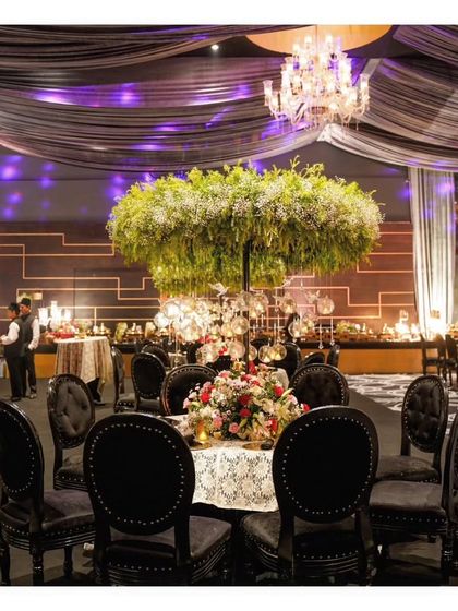A round table setting at a grand event, featuring a stunning, oversized floral arrangement that serves as a beautiful focal point.
