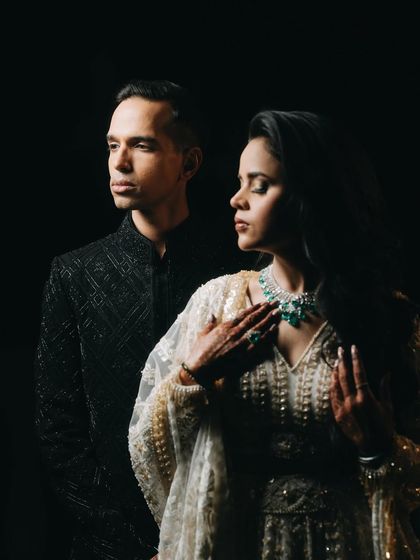 A dramatic and moody portrait. The dark background and focused lighting create an intense, intimate atmosphere, drawing all attention to the couple's elegant attire and serious, connected expressions.
