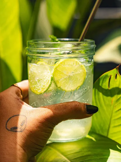 A hand holding our refreshing lime soda against a backdrop of green leaves, capturing the essence of summer.