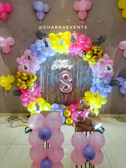 A vibrant Rapunzel-themed birthday party. The circular balloon arch in bright colors frames a shimmering backdrop, with a neon 'Happy Birthday' sign and a light-up number '8'.