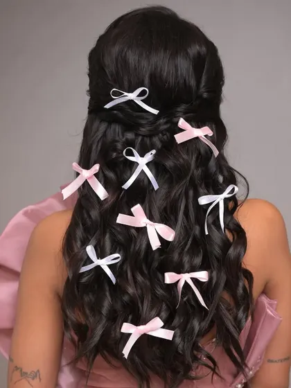 A whimsical and romantic open hairstyle featuring soft waves decorated with multiple small pink and white bows. This look is perfect for a playful and feminine fashion shoot.