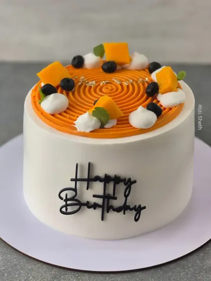 A beautiful Alphonso mango cake with a spiral piping design on top. It's decorated with fresh mango chunks and blueberries for a simple, elegant look.