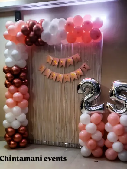 A simple yet elegant balloon arch for a 25th birthday. The color scheme of rose gold, pink, and white, paired with large silver foil numbers, creates a beautiful frame for photos against a shimmering tinsel backdrop.