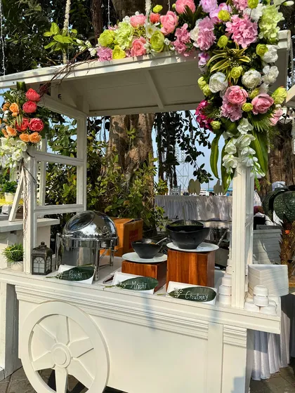 A single white food cart, elegantly decorated with a cascade of flowers. This versatile setup can be used for a variety of food stations, from appetizers to desserts.