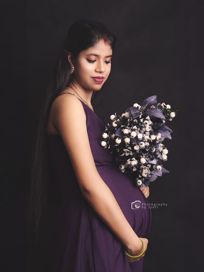 A thoughtful and serene portrait against a black background. The mom-to-be holds a bouquet, adding a touch of softness to the image.