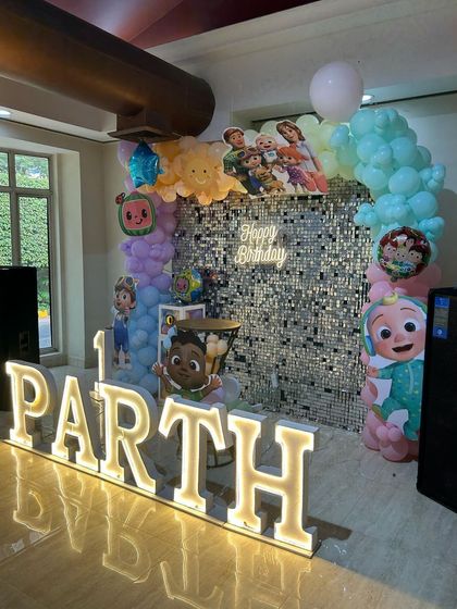 A Cocomelon theme for Parth's 1st birthday, featuring a shimmering silver sequin wall, pastel balloon arch, and large, illuminated letters spelling out his name.