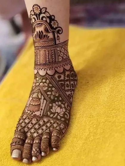 An elegant foot mehndi design featuring a hanging jhumka and lotus motifs. The pattern covers the top of the foot and ankle, leaving the toes open for a modern touch.