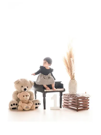 A little girl sits at a miniature piano, surrounded by teddy bears. This charming and creative studio setup captures a playful moment, celebrating her first birthday with a musical theme.