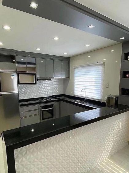 A G-shaped kitchen with a black granite countertop that extends into a breakfast bar. The textured white tiles on the bar front and backsplash add a unique decorative element to the design.