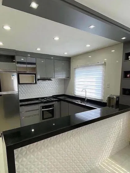 This kitchen features a raised breakfast bar with a decorative 3D-paneled front, adding a unique design element. The grey cabinets and black countertop provide a sleek and modern look.