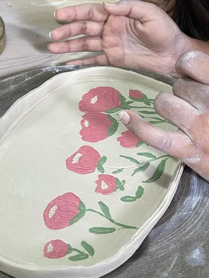 Here you can see the delicate process of hand-painting a floral design onto a custom platter. Each brushstroke is carefully applied to bring the artwork to life before it's glazed and fired, ensuring the design is permanent and food-safe.
