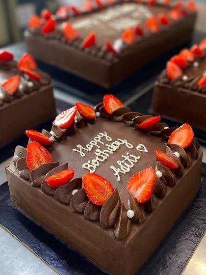 A batch of custom chocolate birthday cakes ready to go. Each one is personalized with a name, like this one for Aditi, and topped with fresh strawberries.