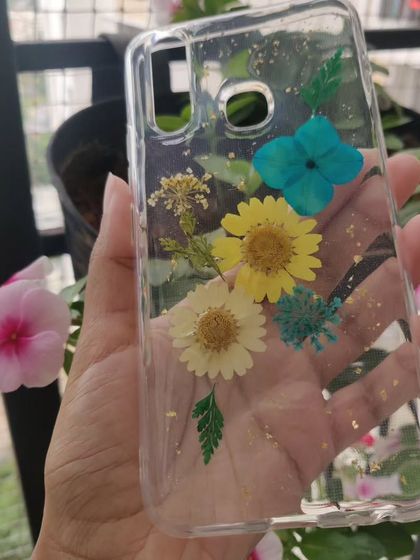 This custom phone case features a bright and cheerful arrangement of real dried flowers, including yellow daisies and blue hydrangeas, with a sprinkle of gold flakes.