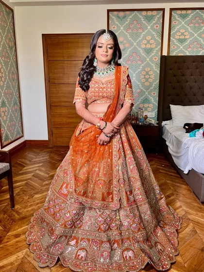 A full view of Shikha's stunning orange lehenga. The makeup was designed to create a royal glow, with a luminous base and soft eye makeup that balanced the vibrant color of her outfit.