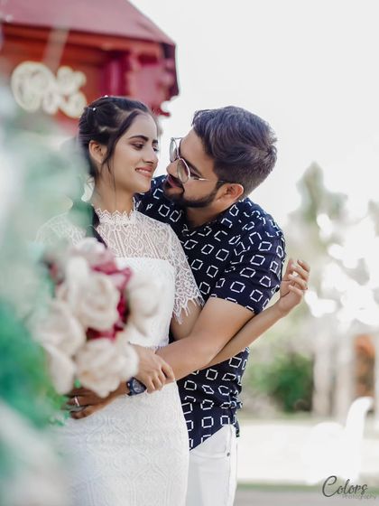 A sweet portrait of a couple in a white-themed outfit, framed by a soft foreground blur.