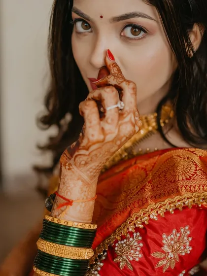 A creative close-up focusing on the bride's henna-adorned hand and her striking red nails, with her face softly blurred in the background.