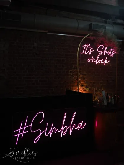 Quirky neon signs for the bar area, including the couple's hashtag #Simbha and the playful phrase "It's Shots o'clock".
