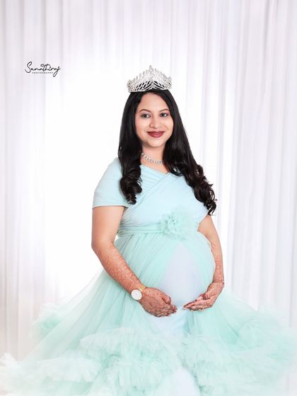 A classic portrait of a mother-to-be in a mint green gown, wearing a tiara. The simple white background and her radiant smile make this a timeless and elegant image.
