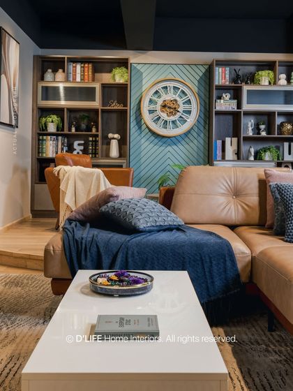 A cozy living room corner featuring a tan leather sofa, custom bookshelves, and a striking teal accent wall with a herringbone pattern. The space is warm, personal, and full of character.