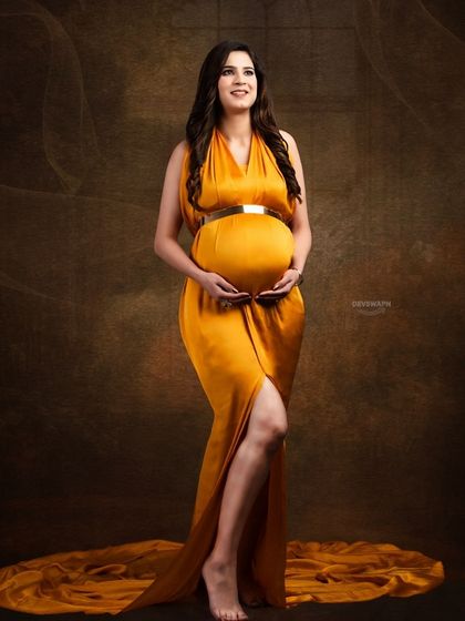 A classic full-length portrait in a mustard-colored gown. The simple pose and dark, textured background create an elegant and sophisticated look that focuses on the beauty of the mother-to-be.